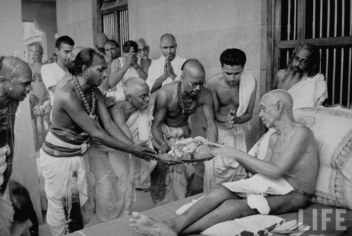 Seated+on+his large stone divan, Sri Ramana Maharshi Receives an off ering of fruit. The offering is being offered by a visiting delegation of Hindu priests from the huge ancient temple in the nearby town of Tiruvannamalai