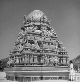 Temple dome swarms with brightly painted statuary. Arrow shows the seated figure of the youthful Sri Ramana.
