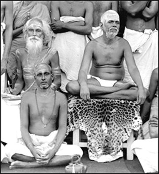 Yogi Ramiah sitting on the ground, B.V.Narasimha Swami behind him, with pencil and paper. Circa 1929